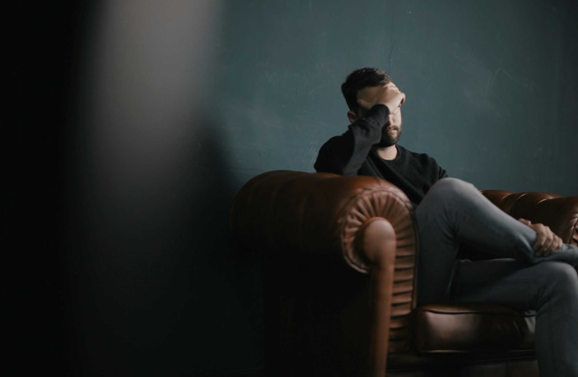 a-man-holds-his-head-while-sitting-on-a-sofa.jpg a man holds his head while sitting on a sofa